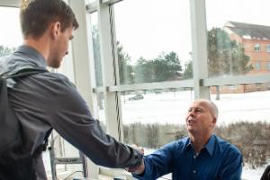 man sitting at table shaking hands with standing student